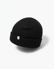 TravisMathew Cloud Beanie in black – minimalist rib-knit winter hat with small woven logo tag, shown on a clean white background.