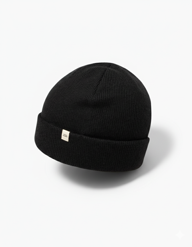 TravisMathew Cloud Beanie in black – minimalist rib-knit winter hat with small woven logo tag, shown on a clean white background.