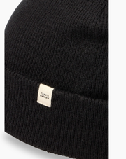 Close-up of the TravisMathew Cloud Beanie in black – rib-knit fabric detail with woven logo label, displayed on a white background.