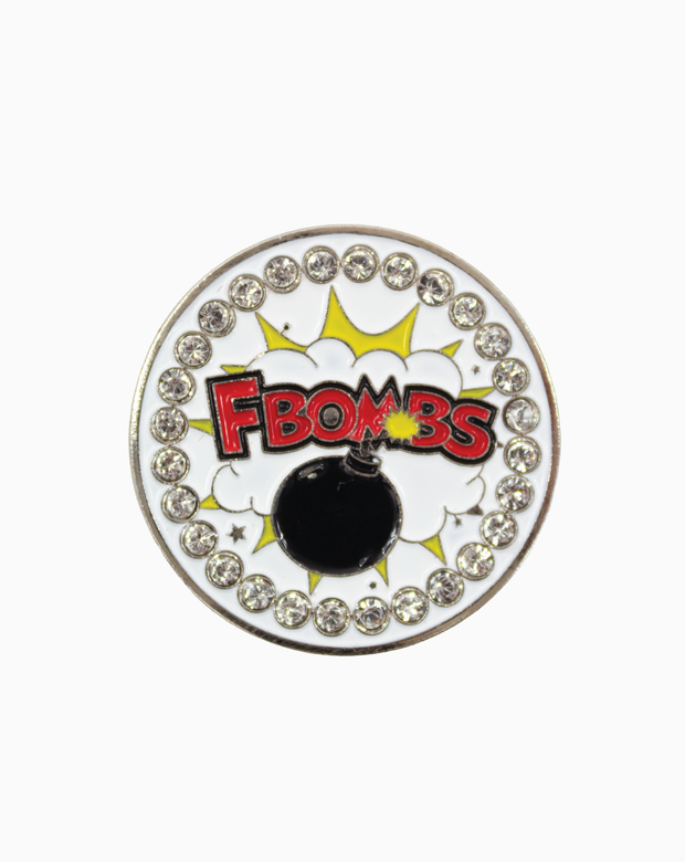 A round MXM ball marker with the text “F Bombs” in red comic-style lettering over a white explosion graphic, featuring a black bomb design and a crystal-studded border.